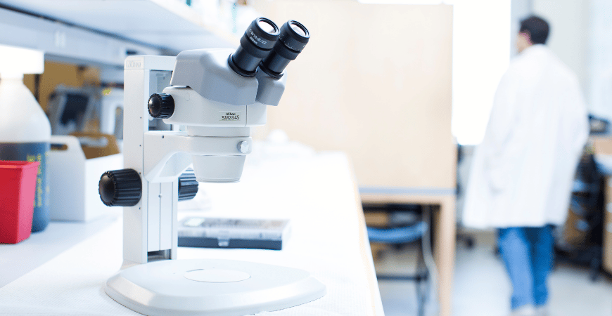 Microscope on lab bench with researcher in background.
